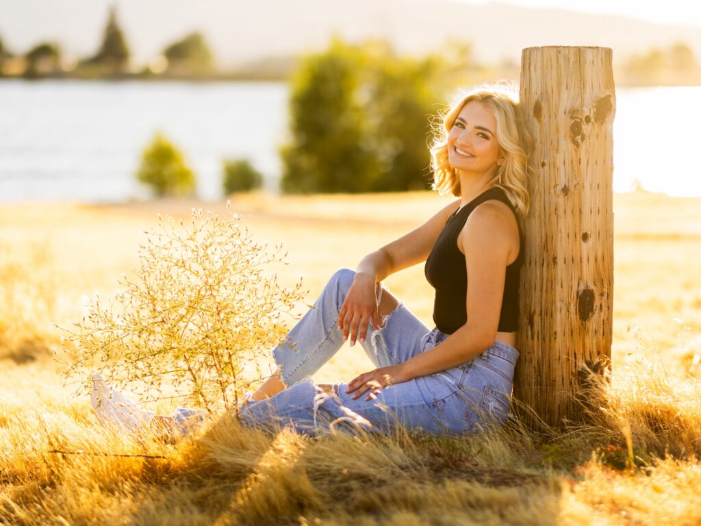 A high school senior portrait of a girl wearing a casual outfit with tank top and jeans in tall hay grass in Vancouver Washington