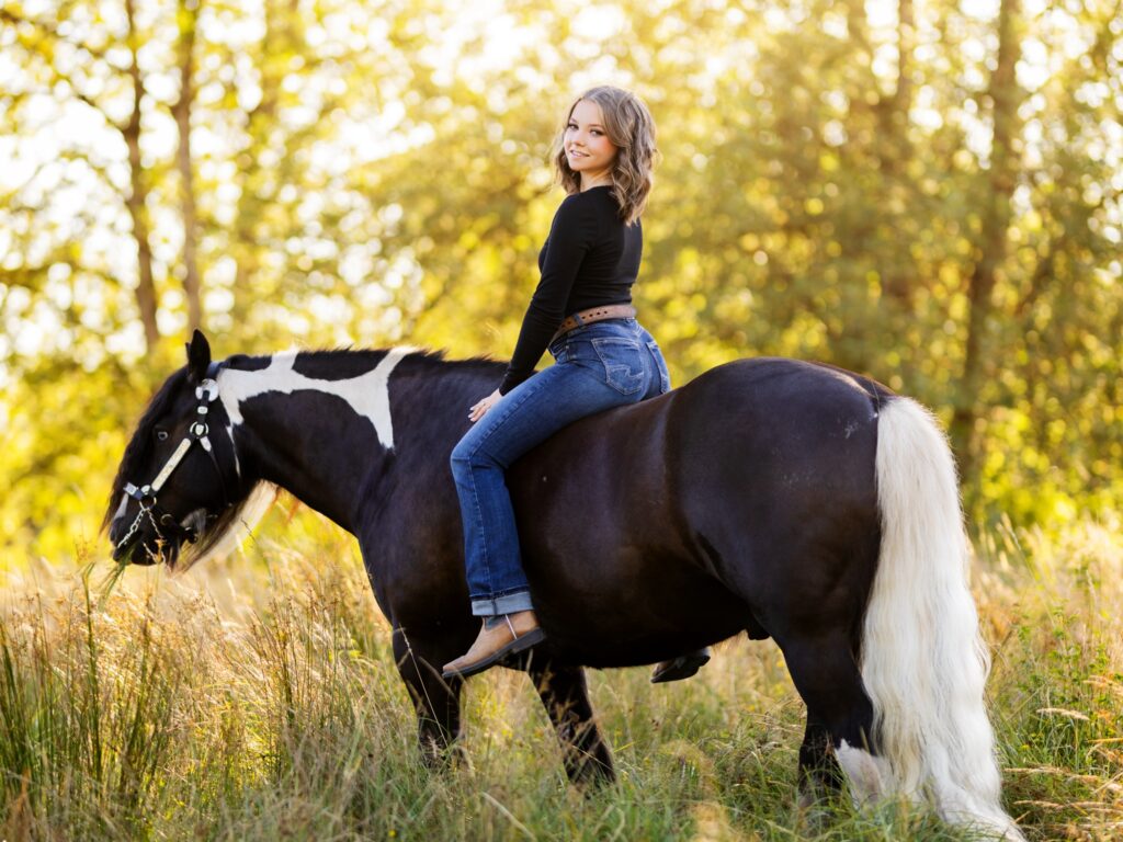 Equestrian horse photos in a country setting with grass and a barn with a high school senior for their senior portraits