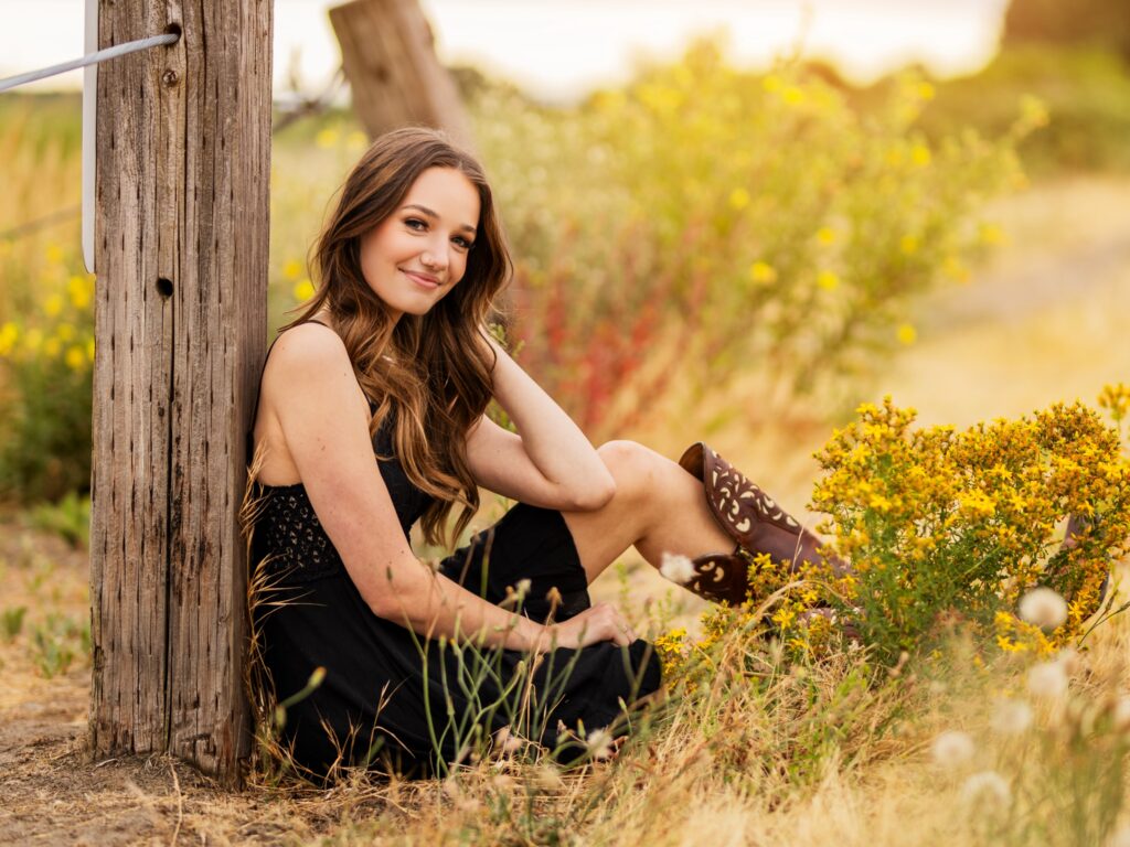 High school senior portraits in downtown Vancouver Washington in a natural setting leaning against a fence post in grasses in a black dress