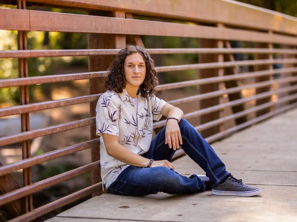 Guy senior portraits in Camas Washington in a nature and forested setting on a bridge over water in a t-shirt and jeans