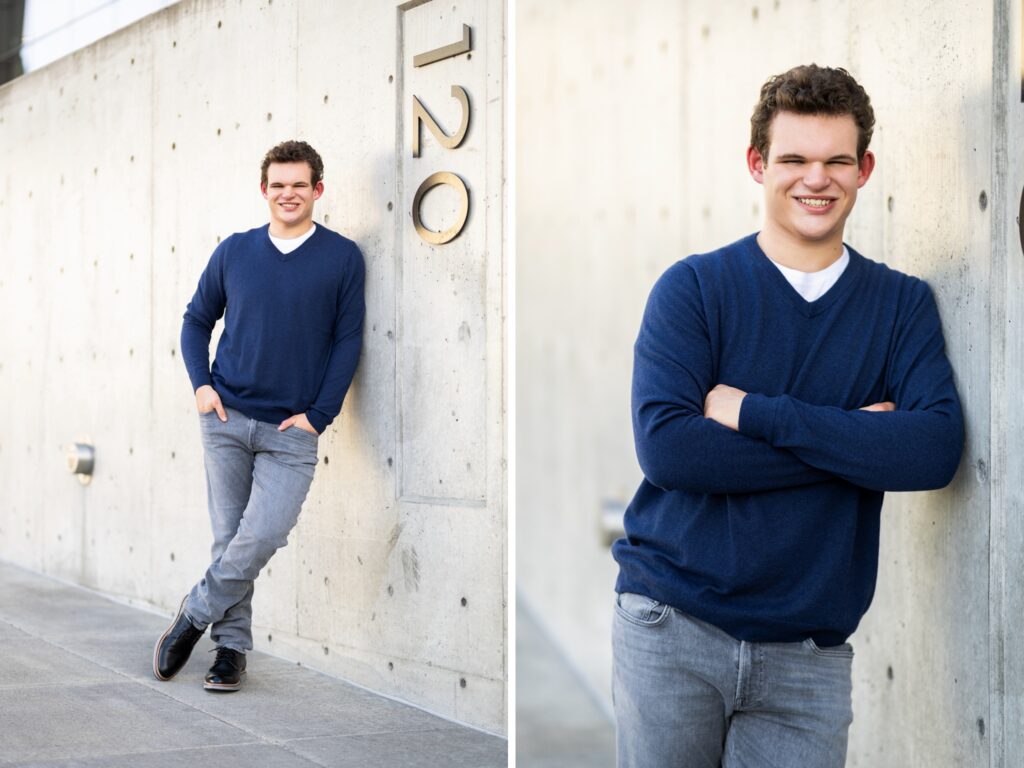 Guy senior photos in downtown Portland, OR wearing a blue sweater, gray jeans, and black dress shoes against a concrete wall.