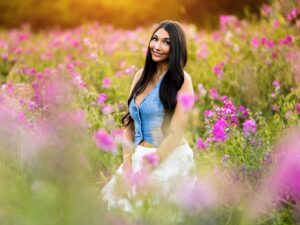 Girl senior photos in a purple sweet pea flower field wearing a denim top and white skirt at golden hour.
