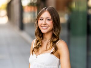 Girl senior portrait in the Pearl District of Portland, OR wearing a white top and jeans with a modern city background.