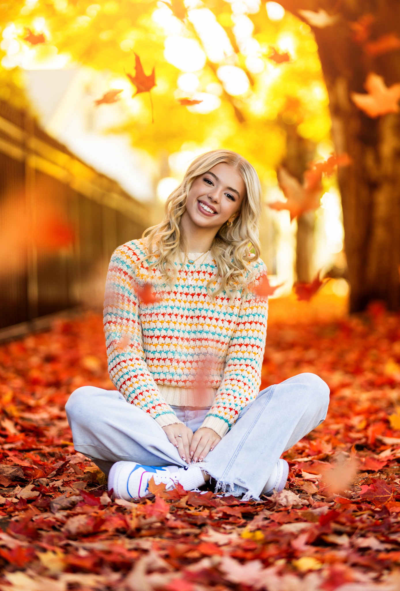 Girl senior photos in downtown Vancouver, WA during fall with colorful autumn leaves wearing a multicolored knit sweater and light wash jeans.