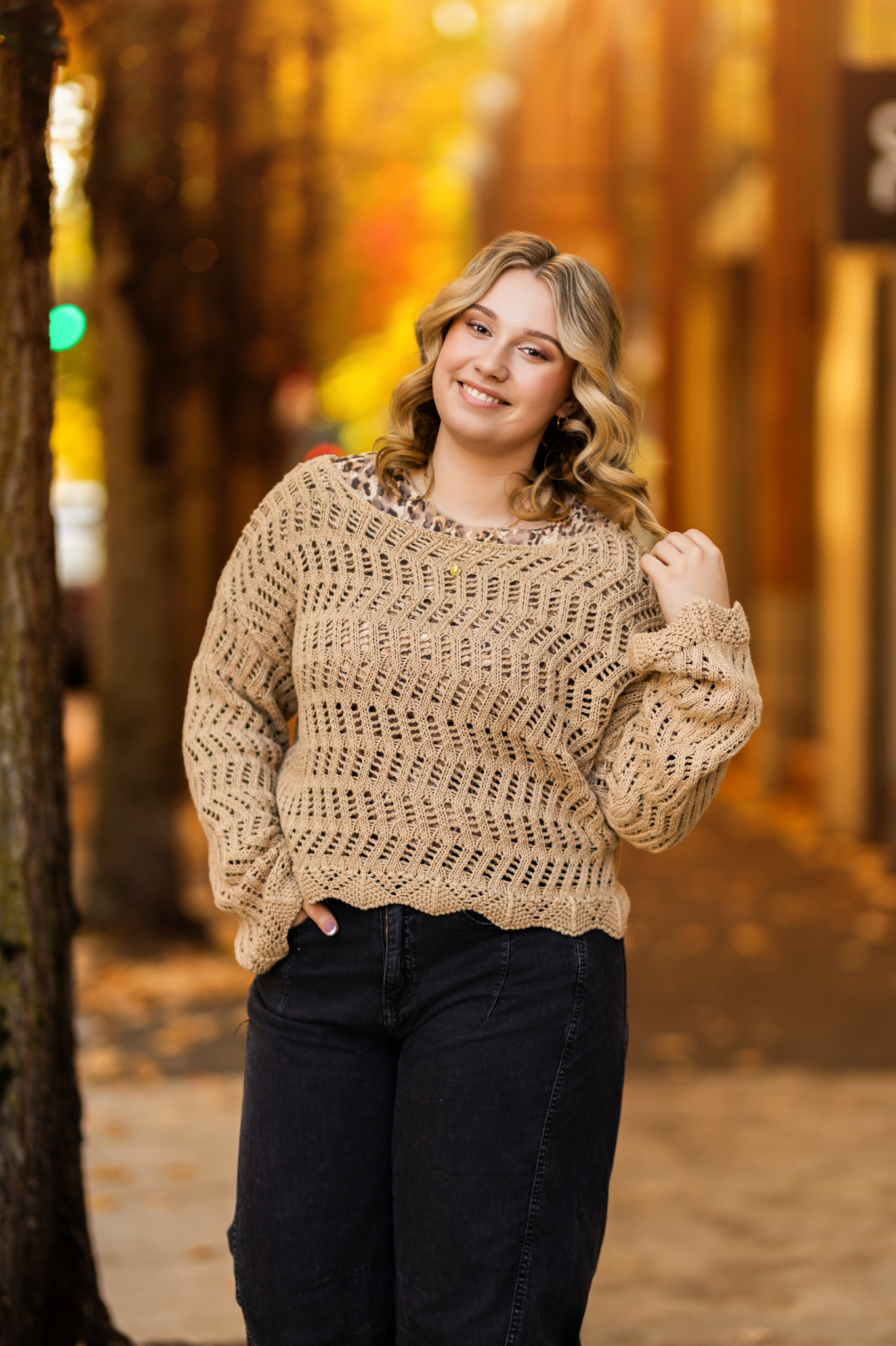 Girl senior photos in downtown Portland, OR during fall with colorful autumn leaves wearing a tan knit sweater over a leopard print top.
