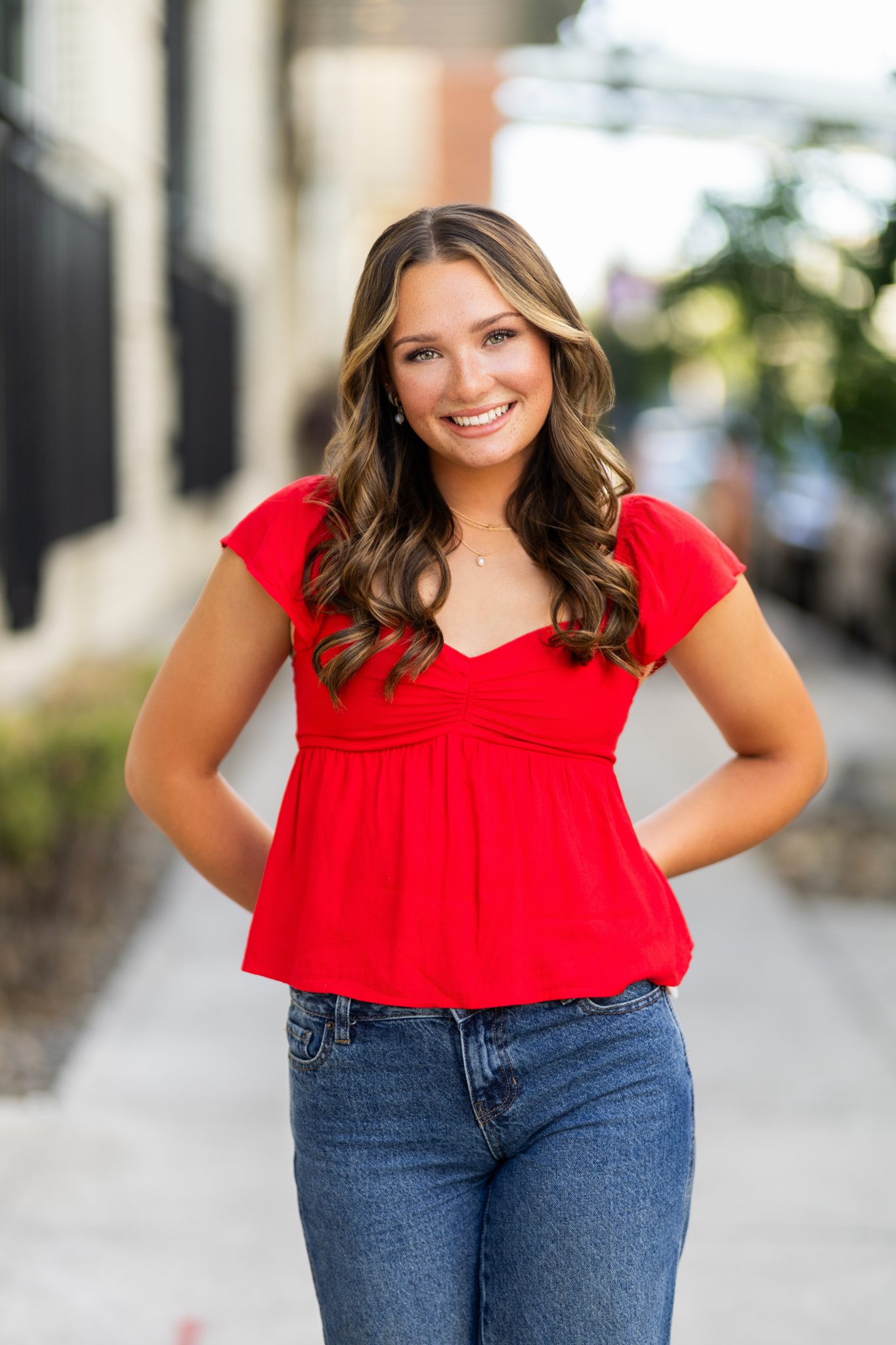 Girl senior photos in downtown Portland, OR during early summer wearing a red cap sleeve top, wide leg jeans, and red and white sneakers on a city sidewalk.